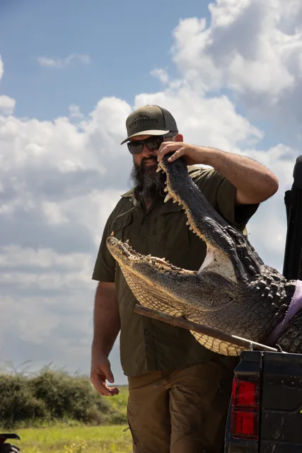 Customer posing beside the open jaw of a harvested alligator on a utility vehicle