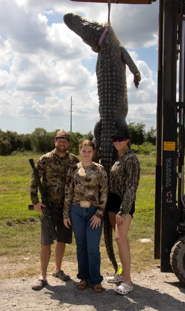 Three visitors posing beside a harvested alligator suspended beside the shop