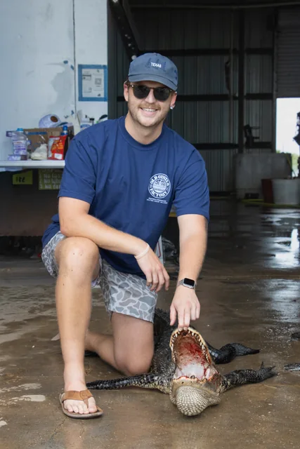 Customer in a blue shirt kneeling beside his alligator at the shop