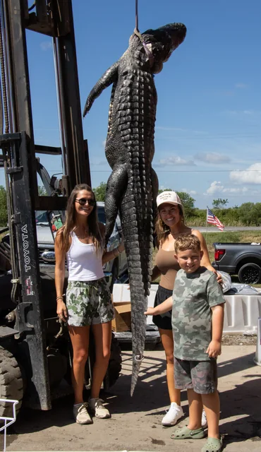 Three visitors standing beside a suspended alligator outside the barn